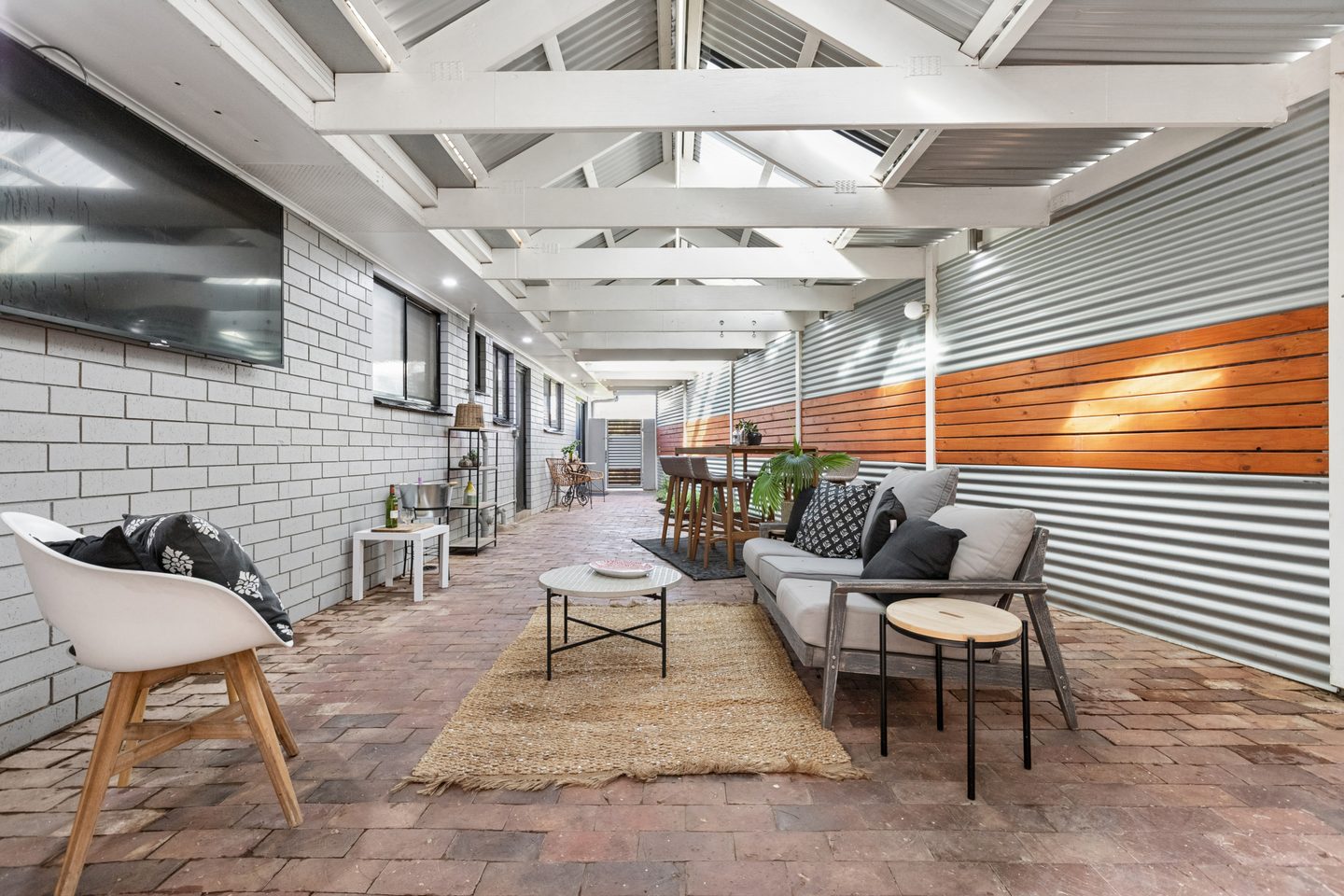 View along the brick-paved covered patio with timber and corrugated metal screening